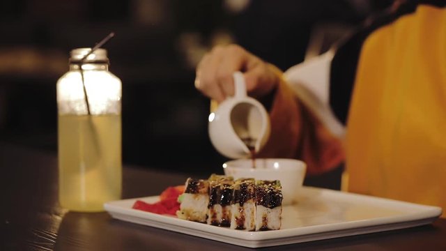 Girl pours soy sauce on Japan restaurant, eating sushi set with chopsticks close up