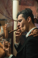 Man smoking cigar and drinking whiskey at night in a company with pretty girls