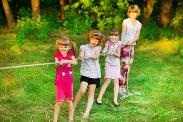 Fototapeta premium Group of happy children playing tug of war outside on grass. Kids pulling rope at park.