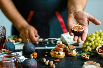 Figs fruit in hands in the kitchen. Bruschettas with figs, Blue cheese and walnuts on grilled crusty bread. Food recipe concept