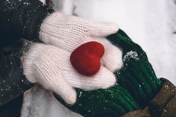 Hands in gloves holding heart closeup on winter snow background. Toned. Valentine's Day and love concept