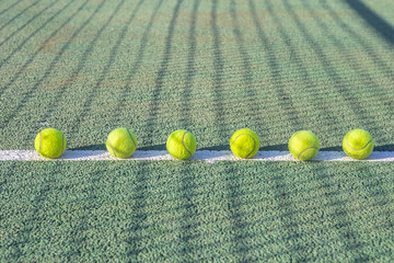 Tennis balls laid out in a row on a white line on a tennis court