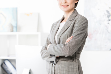 cropped image of businesswoman in grey suit standing with crossed arms in office