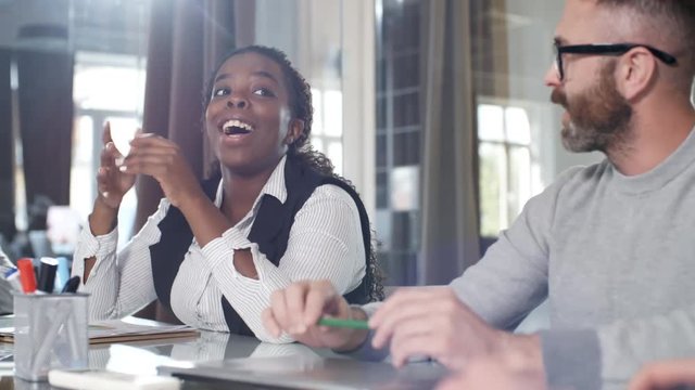 Medium shot of young black woman smiling when talking to male colleague during meeting in office