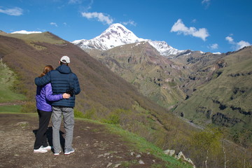 Fototapeta na wymiar Man and woman stand embracing and look at the snow-capped peak