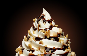 Whipped cream, frozen yogurt or soft ice cream with chocolate sauce and hazelnuts isolated on black...