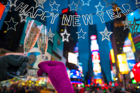 Happy New Year scene with silver banner hanging above hands giving a Champagne toast in front of the bright lights of Times Square, New York City