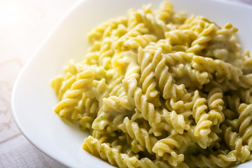 Closeup of a plate of fusilli pasta with green pesto sauce