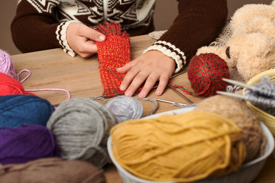 Child boy is learning to knit. Colorful wool yarns are on the wooden table. Hand closeup.