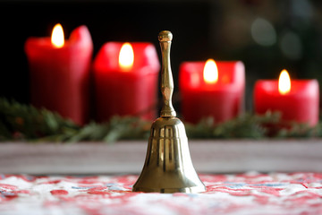 Goldene Hand Glocke aus Messing mit brennenden, roten Kerzen an Weihnachten