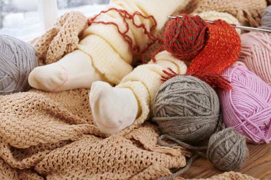 Child legs in warm socks are on a window sill with wool yarns.
