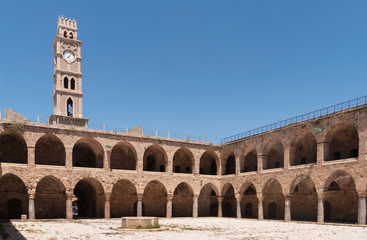 the khan al umdan caravanserai in acre akko israel showing the courtyard and clock tower with a clear blue sky