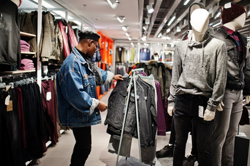 Stylish casual african american man at jeans jacket and black beret at clothes store looking on new...