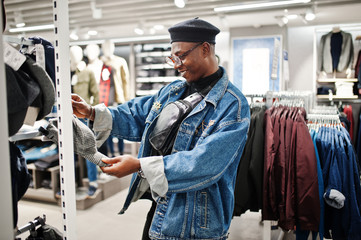 Stylish casual african american man at jeans jacket and black beret at clothes store looking on new cap.