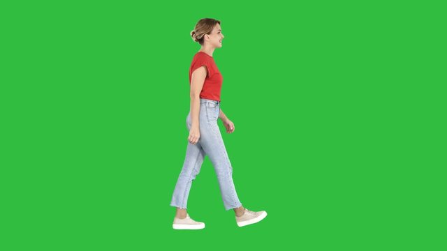Woman in red t-shirt, jeans and sneakers walking on a Green Screen, Chroma Key.