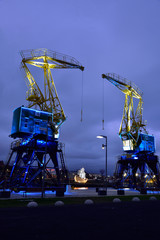 Colorfully illuminated antique cranes on the quay of Szczecin Łasztownia. - obrazy, fototapety, plakaty
