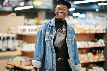 Stylish casual african american man at jeans jacket and black beret holding two baskets, walking and shopping at supermarket.