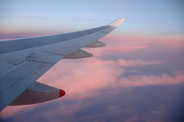 Obraz premium A view from the window of an airplane flying above the clouds during a beautiful sunset. Visible wing of the flying aircraft.