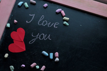 I love you, written chalk on a blackboard. Happy Valentines Day. Valentine's Day theme. Mother's Day. Chalk lettering on blackboard with paper red hearts. Colored chalk lying on a black school board