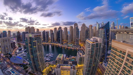 Modern skyscrapers and water channel with boats of Dubai Marina at sunset and day to night timelapse, United Arab Emirates.
