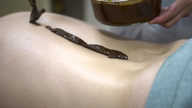 Close up for a patient lying on a bed with hot therapeutic mud on his back, and alternative medicine concept. Close up for male back with hot, liquid herbs mixture, wellness procedure.