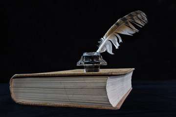 libro antiguo con tintero y pluma de pájaro con fondo negro