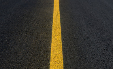 A yellow line in the middle of a black asphalt road. Only the line and road are visible. Focus is on the closest part of the line.