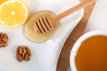 honey in a white ceramic bowl with honey dipper and lemon on a wooden kitchen boar