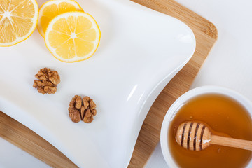 honey in a white ceramic bowl with honey dipper and lemon on a wooden kitchen boar