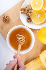 honey in a white ceramic bowl with honey dipper and lemon on a wooden kitchen boar