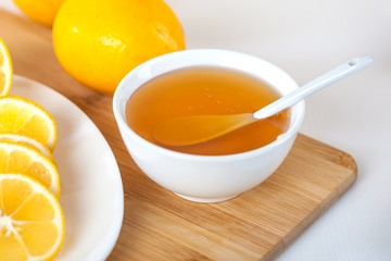 honey in a white ceramic bowl with spoon and lemon on a wooden kitchen board