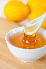 honey in a white ceramic bowl with spoon and lemon on a wooden kitchen board