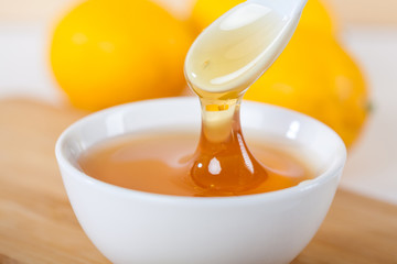 honey in a white ceramic bowl with spoon and lemon on a wooden kitchen board