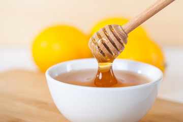 honey in a white ceramic bowl with honey dipper and lemon on a wooden kitchen boar