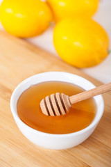 honey in a white ceramic bowl with honey dipper and lemon on a wooden kitchen boar