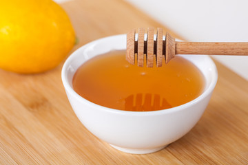 honey in a white ceramic bowl with honey dipper and lemon on a wooden kitchen boar