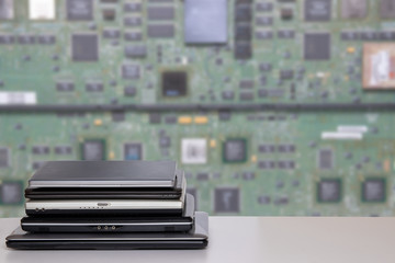 Stack of laptop computers. A pile of computers on a bright table against bright blurred green digital electronic circuit board texture background. PCB. Template for your product display montage.