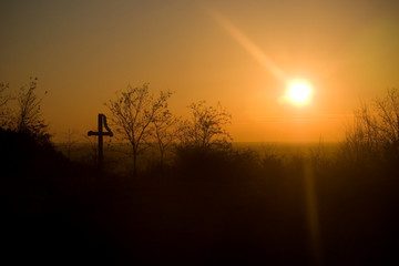 Orange cloudless sunset with silhouette of a cross in the foreground.