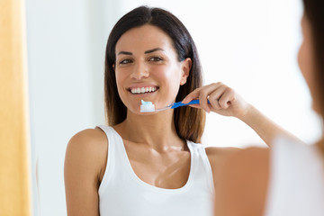 Naklejka premium Pretty young woman brushing her teeth in the bathroom at home.
