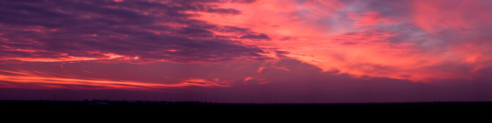 A panorama of dramatic purple pink and orange sunset with wispy clouds.