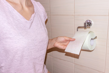 Unrecognizable woman, sitting on a toilet and rewind and tear off a toilet paper. Concept image of digestive problems and difficulties in the toilet