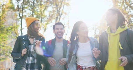 Cheerful Caucasian company of friends students talking and laughing while walking the autumn park on sunshine day. Outside. - Powered by Adobe