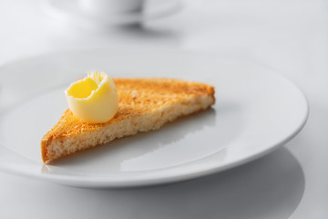 Slices of toasted bread and butter on the white plate and white table. Selective focus.