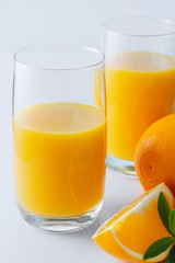 Two glasses of orange juice and oranges with leaves on white background. Close up. Selective focus. Vertical shot.