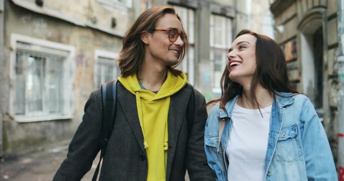 Cute young Caucasian couple of hipsters in love walking the narrow slums street and talking joyfully. Close up. Outdoors.