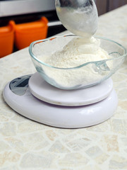 A woman is cooking in her kitchen, about to bake a cake. Weighs flour on small kitchen scales. close-up