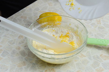 A woman is cooking in her kitchen, about to bake a cake. Woman poured lemon zest into a mixture of chicken yolks, sugar and flour