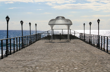 View of an empty pier with a white wedding gazebo, the sky and the glittering Mediterranean sea from the Limassol seafront in December