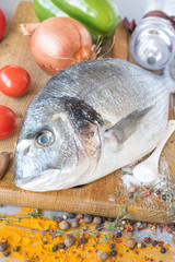 Large carcass  of sea fish dorado   on and wooden board  on and background green-stuffs.