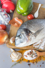 Large fish dishes of Mediterranean cuisine on a wooden board on the background of onion, tomato, sweet pepper. Cooking process.